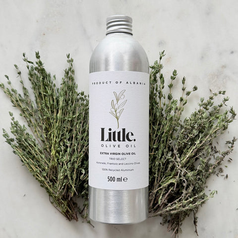 A 500 ml silver aluminum bottle of Little Olive Oil Extra Virgin Olive Oil, surrounded by sprigs of fresh thyme on a white marble background.